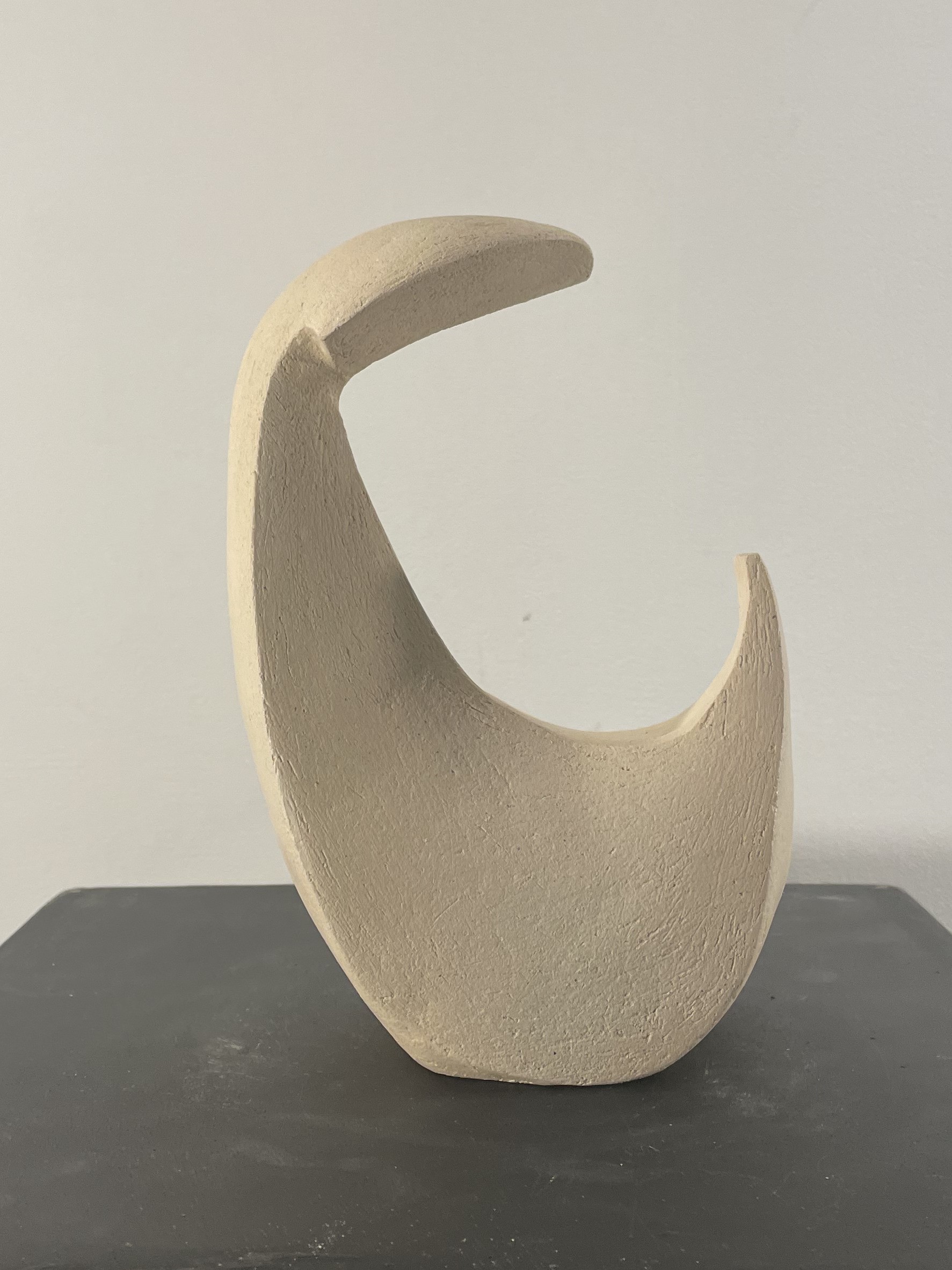 Matte unglazed ceramic crescent sculpture evoking a reader absorbed in a book, warm pale tones